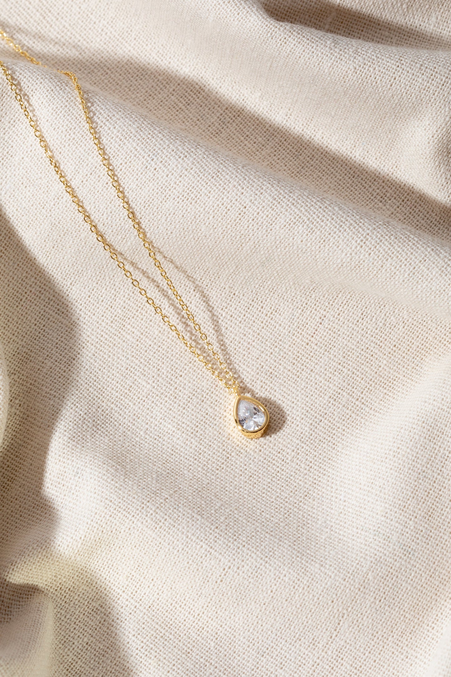 grief pendant on a gold chain. jewellery is on a silk material background