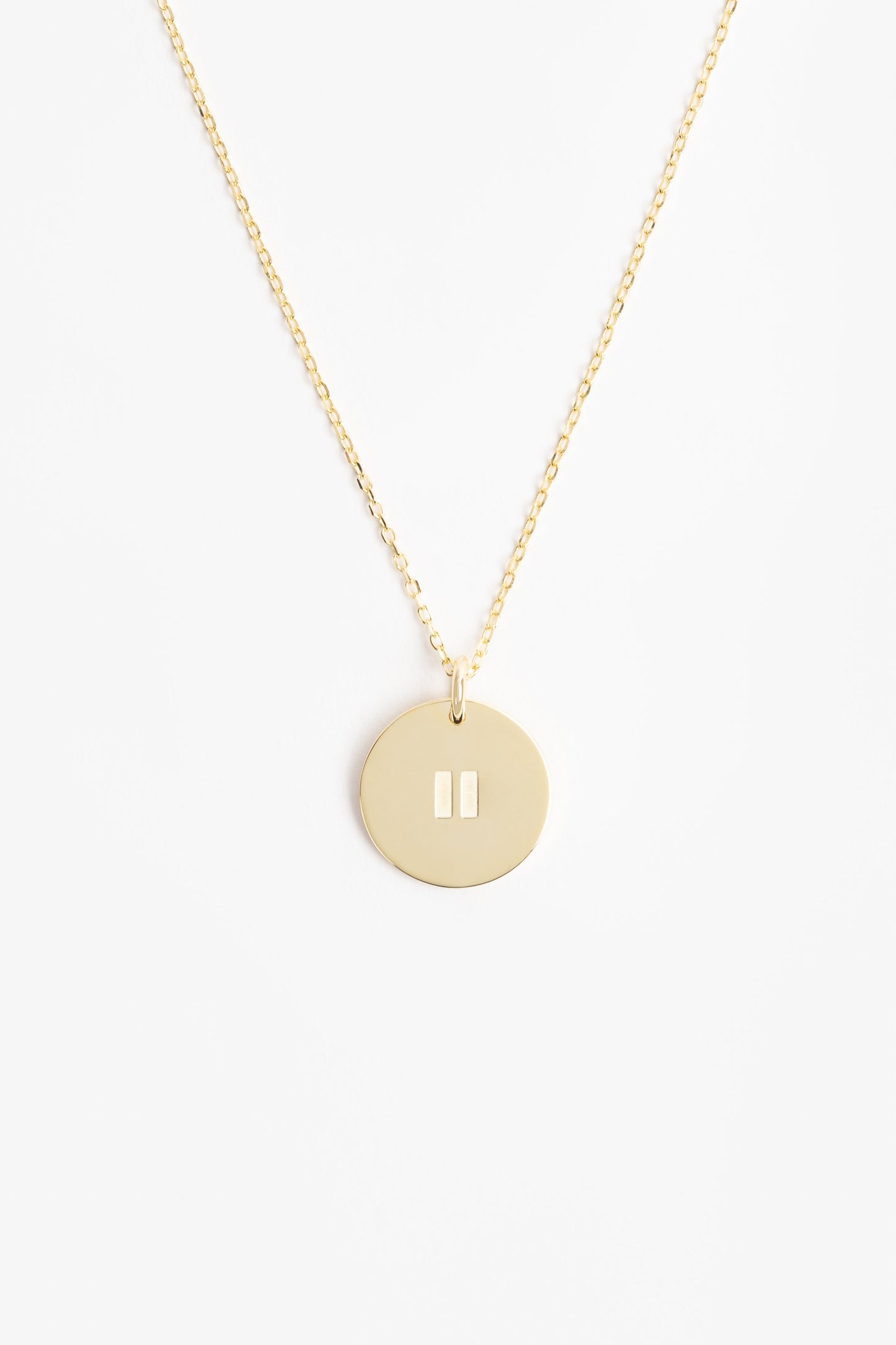 Gold pendant on a gold necklace with a pause symbol on disc. it is on a white background