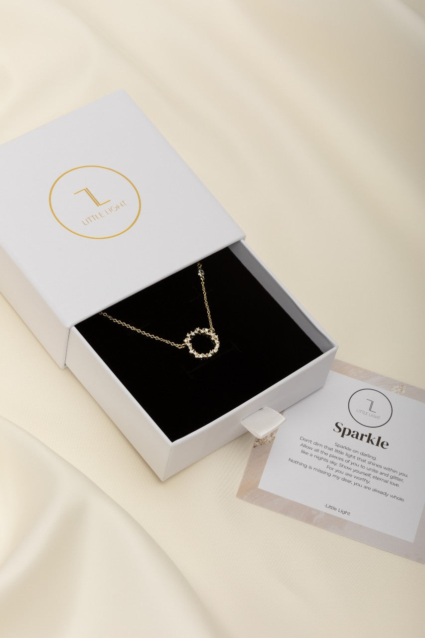 cubic zirconia studded circle pendant on a gold chain displayed in a with box with black foam insert