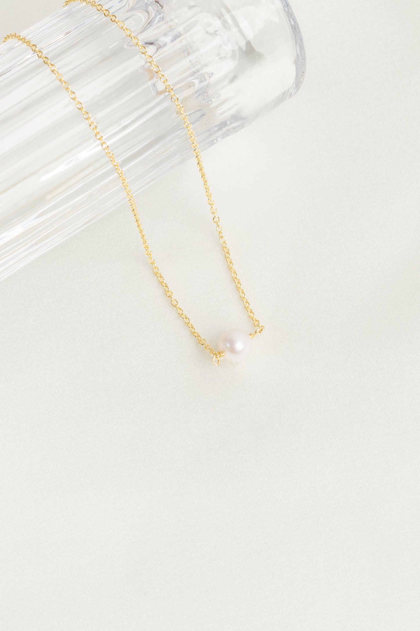 freshwater pearl pendant necklace on a gold chain. displayed draped over a glass on a white background
