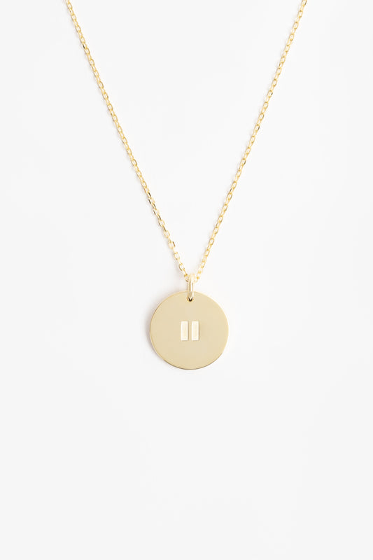 Gold pendant on a gold necklace with a pause symbol on disc. it is on a white background