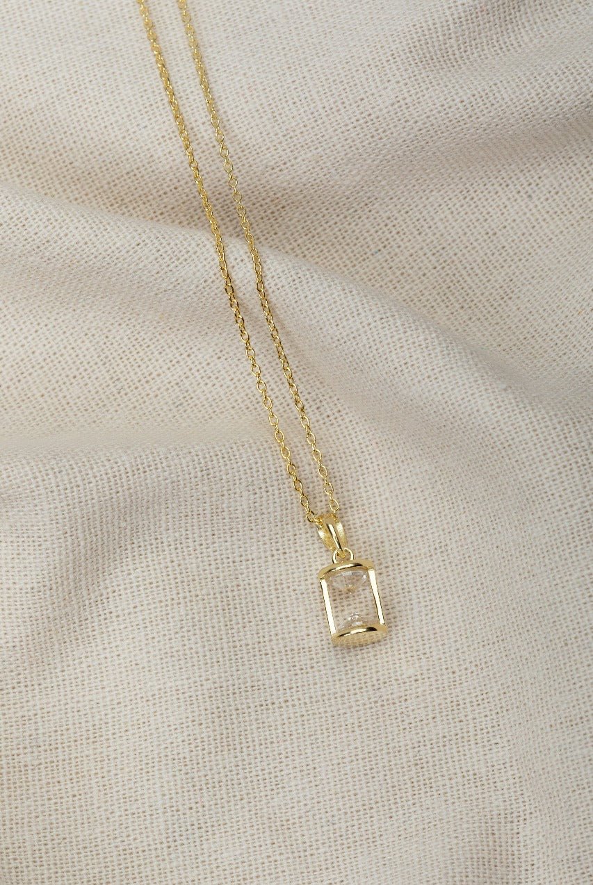 hourglass pendant necklace with two cubic zirconia's on a gold chain. its on a silk background