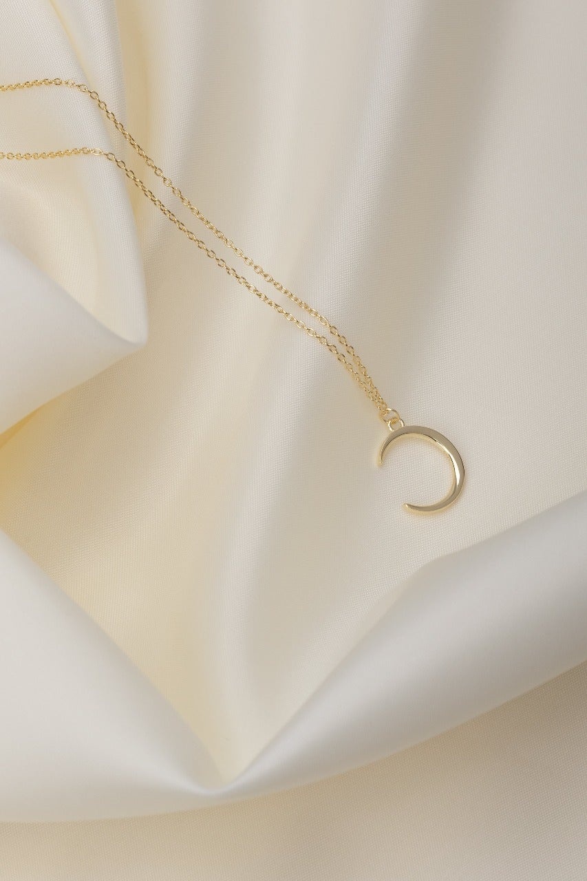 new crescent moon shaped pendant necklace on a gold chain. resting on a silk material