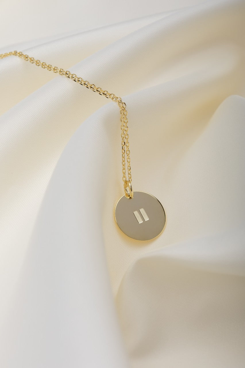 Gold pendant on a gold necklace with a pause symbol on disc