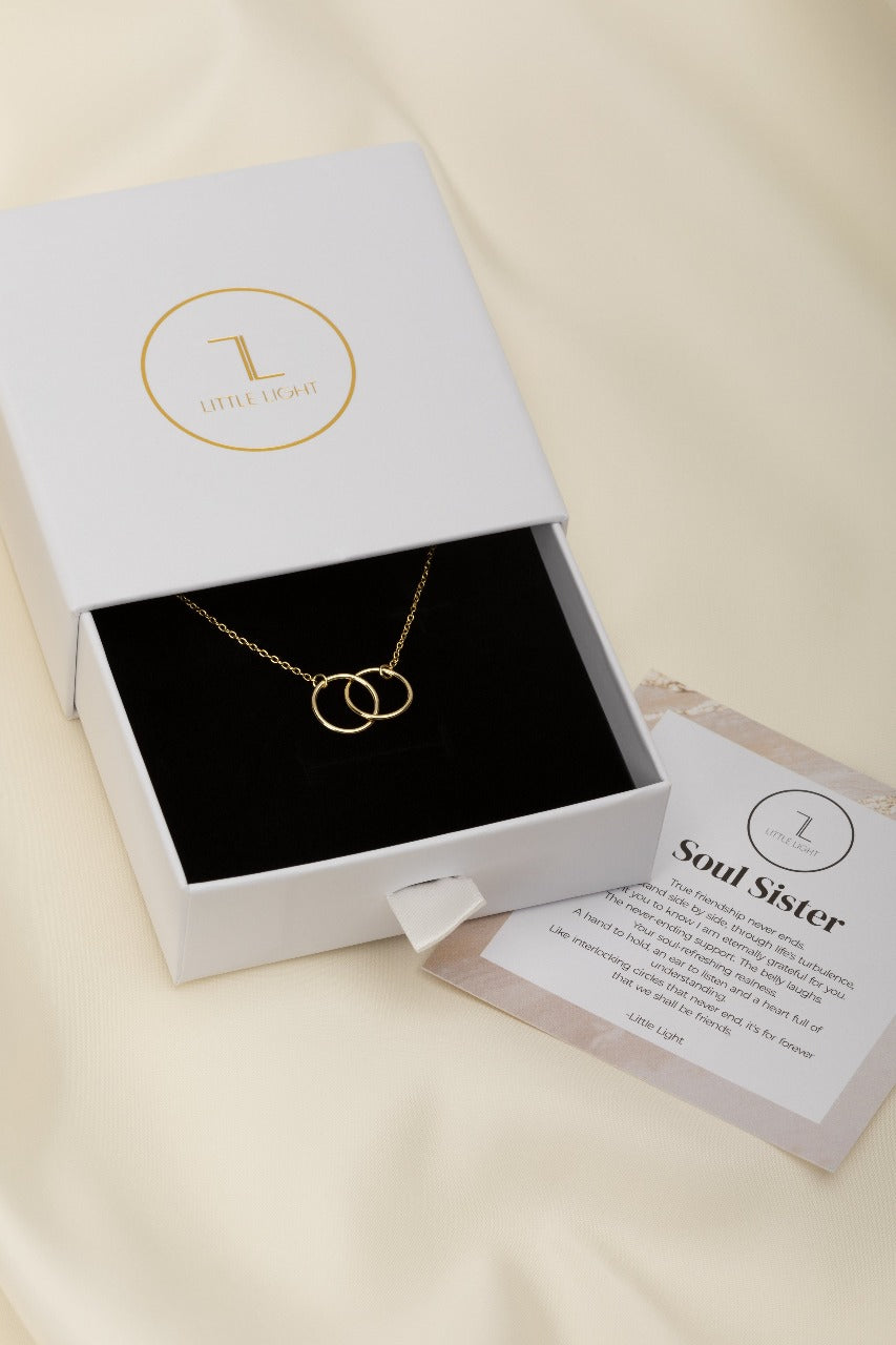 two gold circles on a gold necklace. this image in a white box with a black foam insert 