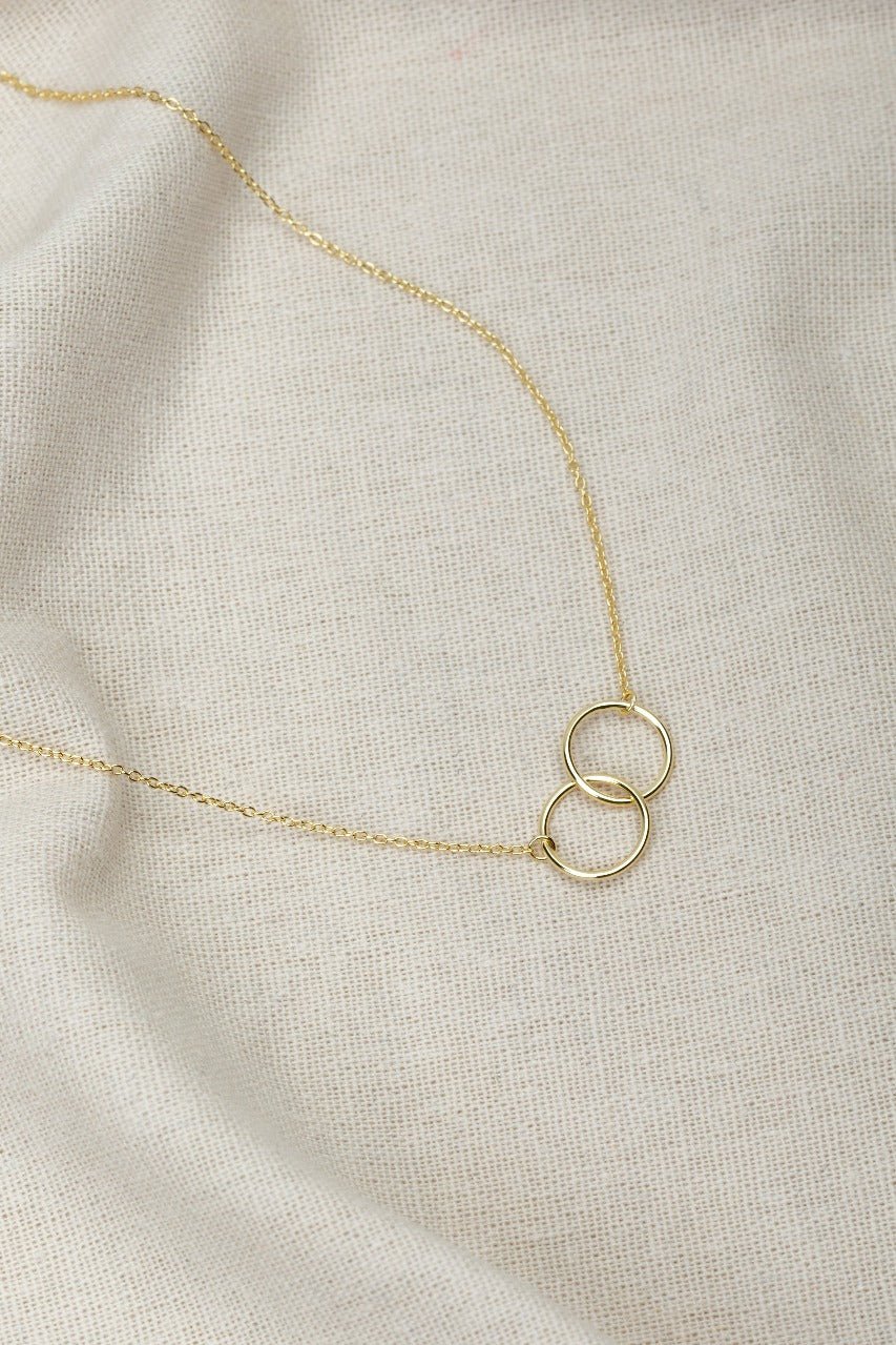 two gold circles on a gold necklace. this image is on a white material background