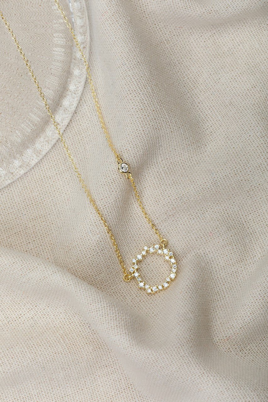 gold chain with a cubic zirconia studded circle pendant displayed on a material background